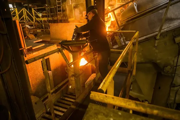 Ouvrier ajoutant un ingrédient vers le métal en fusion via une gouttière