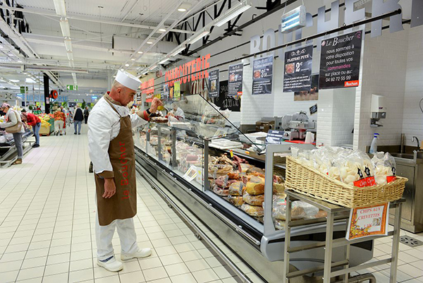 Boucher-charcutier vérifiant sa vitrine dans un supermarché Boucher-charcutier vérifiant sa vitrine dans un supermarché